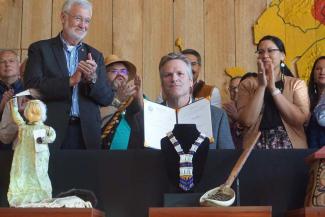 Sen. Gary Stevens and Rep. Tiffany Zulkosky, sponsors of legislation on tribal education and on state recognition of tribes, hold up the bills signed by Gov. Mike Dunleavy at a July 28 ceremony at the Alaska Native Heritage Center. The ceremony attracted a large crowd, including Native leader Emil Notti and Sen. Lyman Hoffman, standing on the stage with Stevens and Zulkosky. (Photo by Yereth Rosen/Alaska Beacon)